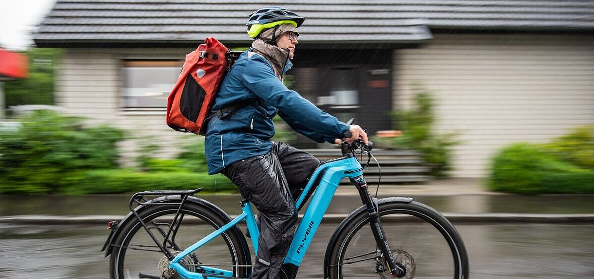 Radfahrer von der Seite aufgenommen auf Pedelec im Regen unterwegs. 